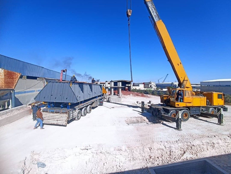 Crane lifting heavy steel equipment from truck